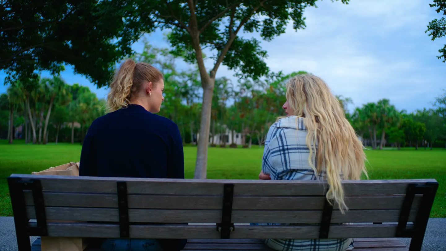 The two of them on a park bench, seen from behind, trees ahead.