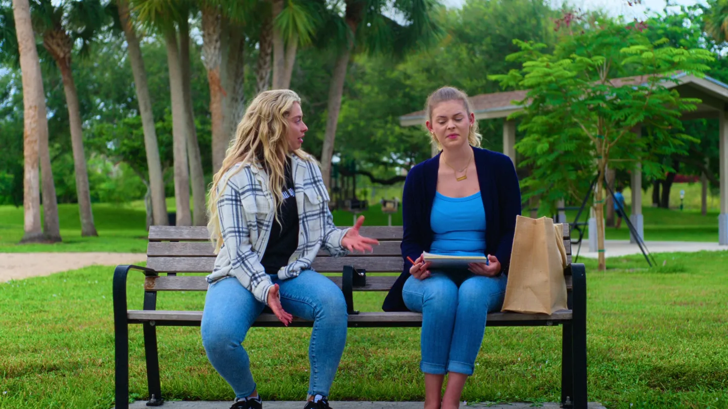 Face to face on the bench: one talks with her hands, the other holds a folder of papers.