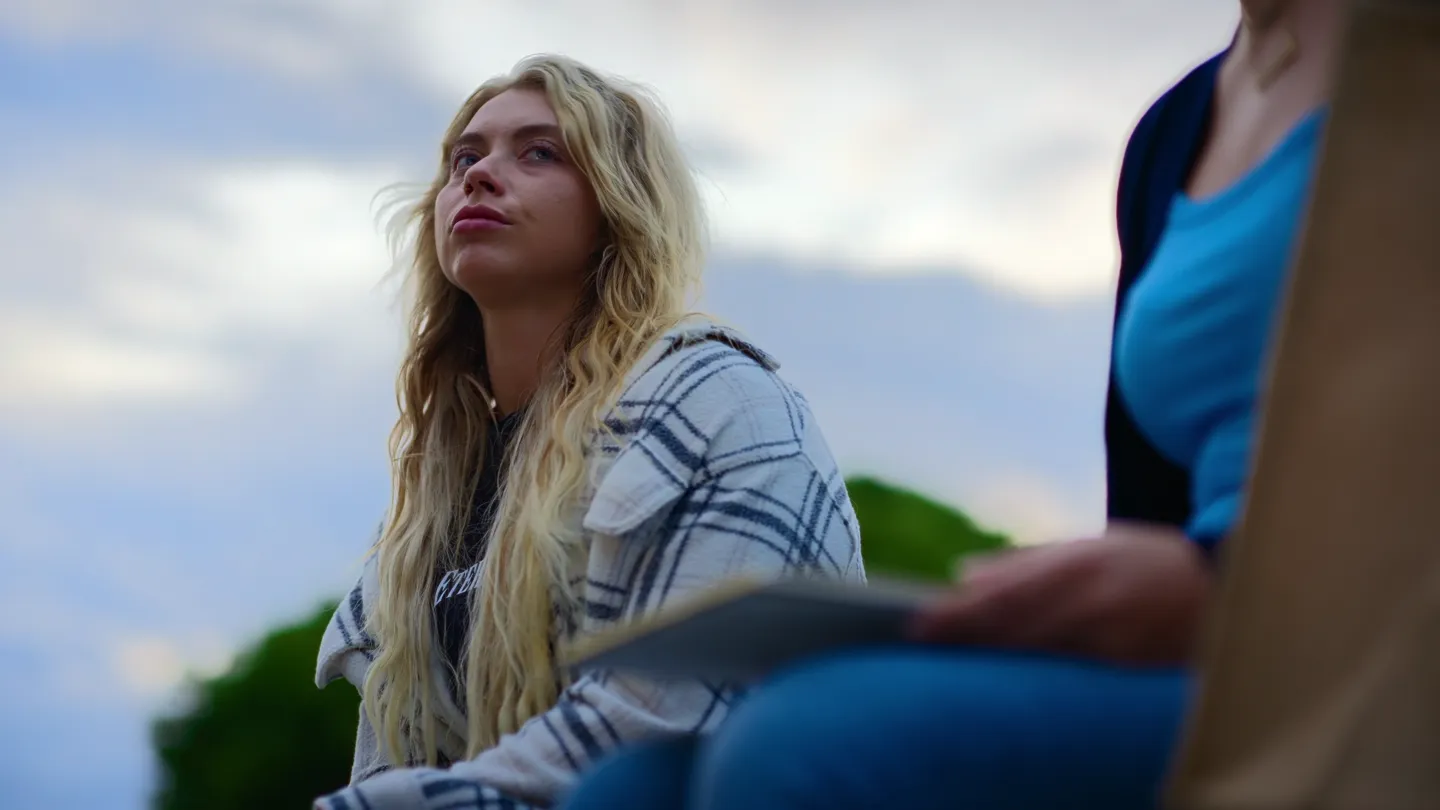 A low angle against a bright sky, the blonde woman looking off, hair in the wind.
